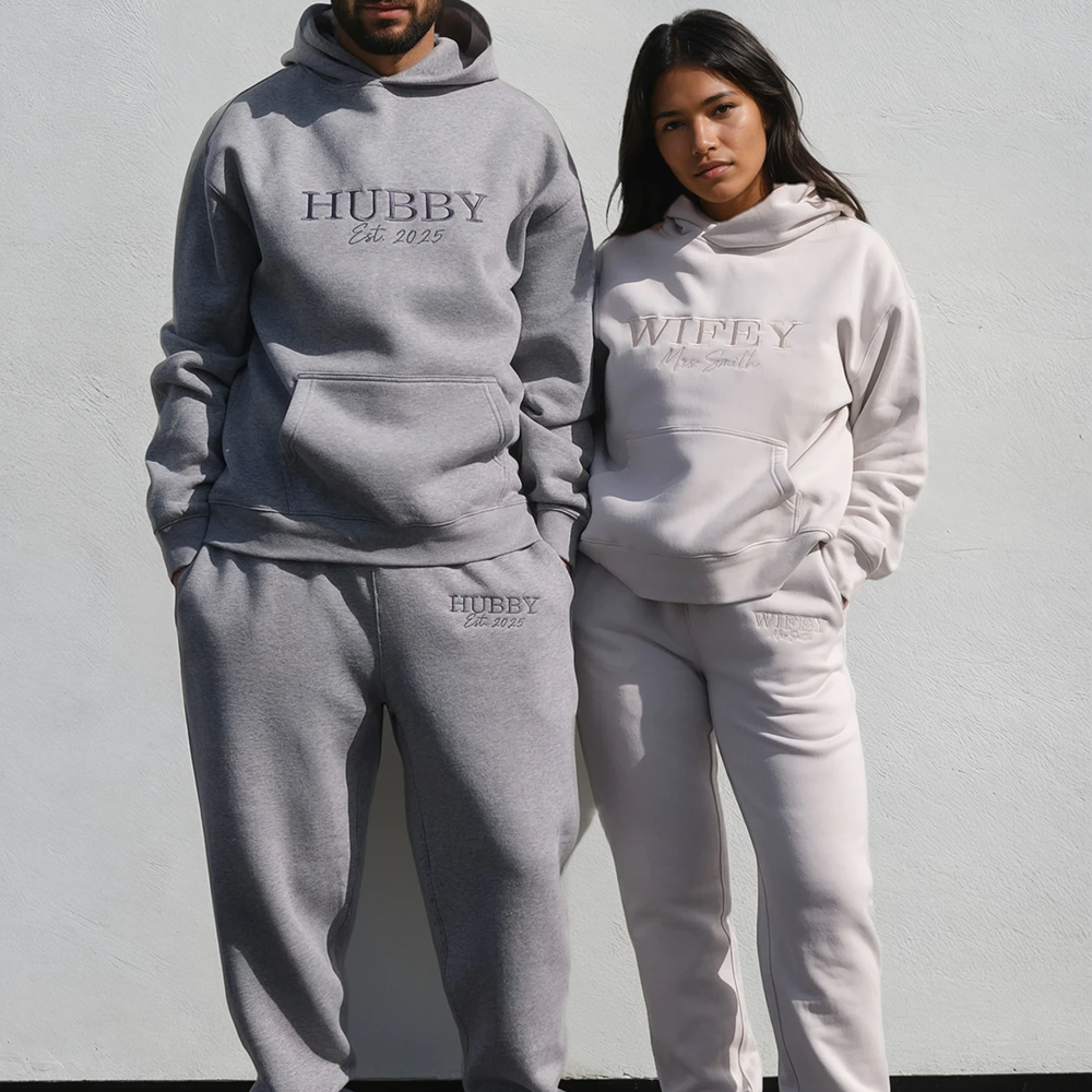 A male and a female model wearing matching hoodie and jogger sets that read HUBBY and WIFEY in statement text