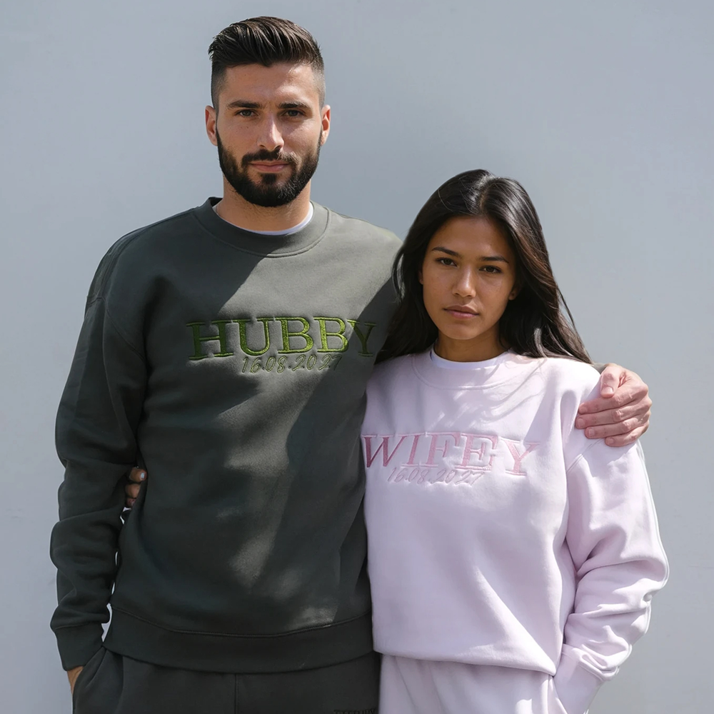 A couple wearing matching honeymoon sweaters in orchid and cypress green