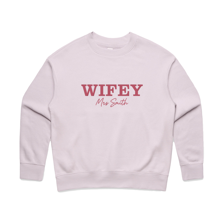 An orchid coloured honeymoon sweatshirt that has WIFEY embroidered on it in a statement font and Mrs Smith underneath 