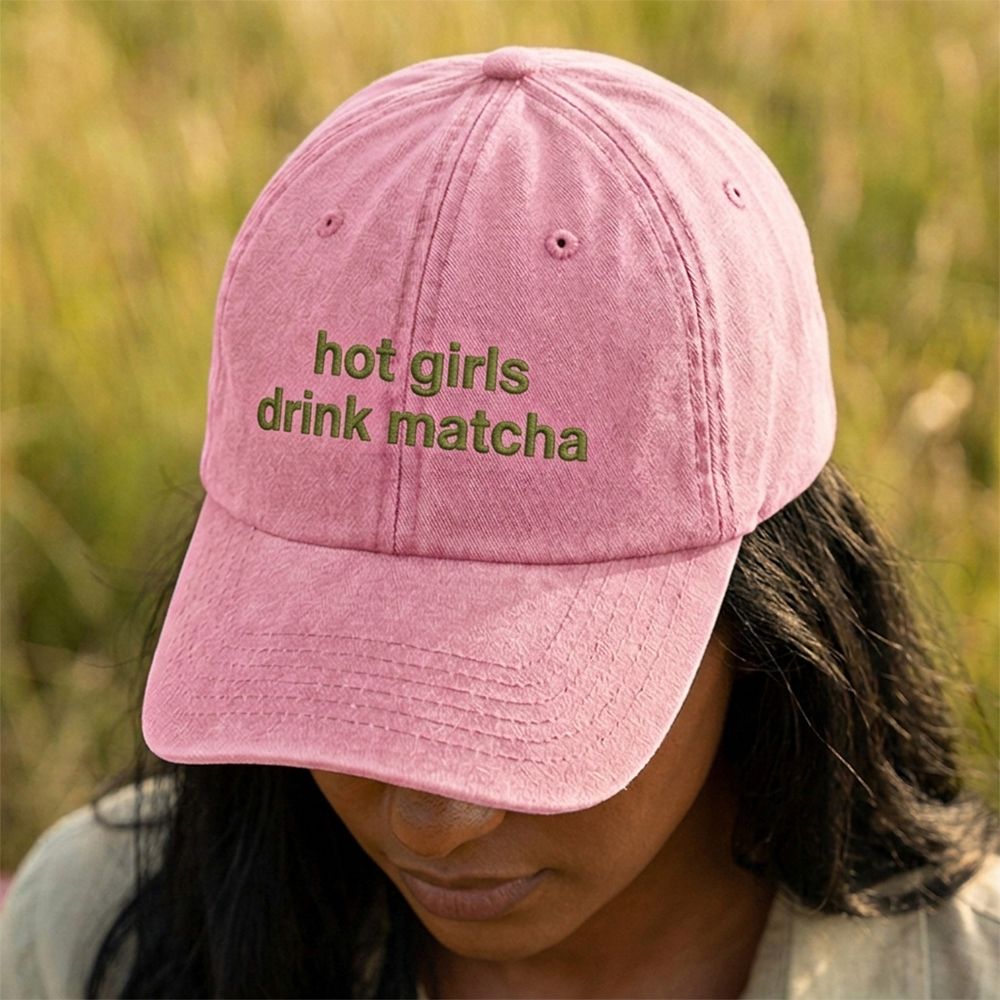 A female model stood in a field wearing a premium hen do cap in pink with custom text hot girls drink matcha embroidered on it