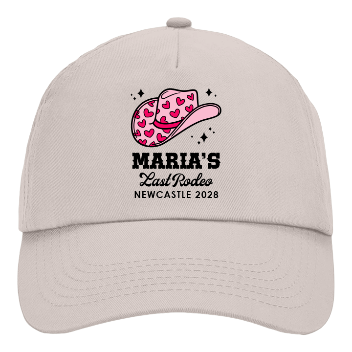 A custom hen do cap which is sand coloured with a design of a pink cowgirl hat with the custom text Maria's Last Rodeo Newcastle 2028