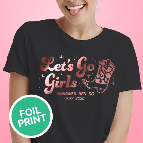 A female model wearing a black hen do shirt with custom shiny foil pink writing that has a cowboy boot on it and reads Let's Go Girls, Morgan's Hen Do, York 2026 