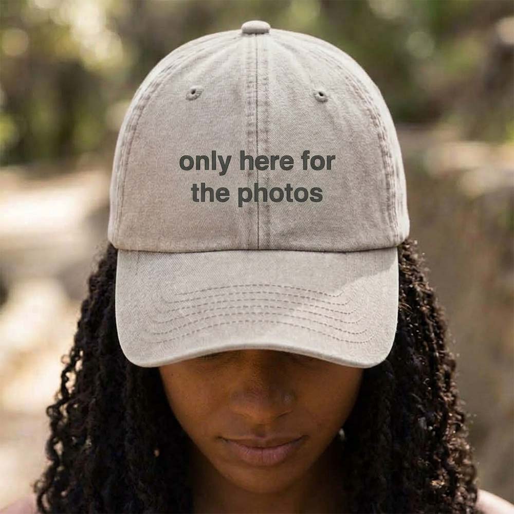 A female model wearing a premium hen do cap in stone that has been embroidered with the phrase only here for the photos in a navy font