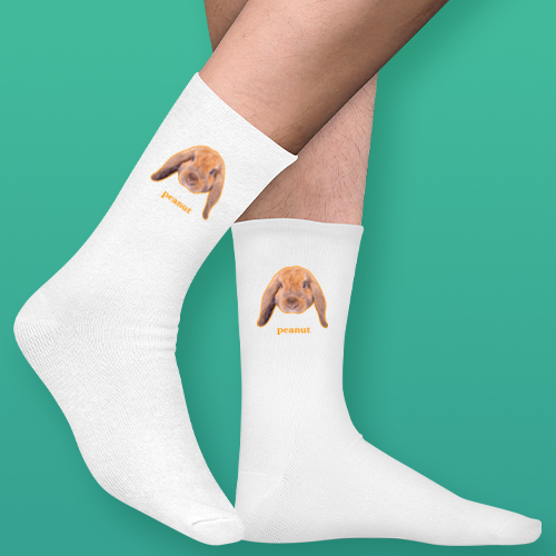 A pair of white socks that can be customised with the face of a pet and up to two lines of custom text that have a picture of a rabbit on each sock with the word peanut underneath it 