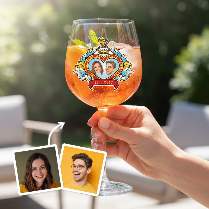 A custom glass with an orange liquid in it boasting a Royal Wedding style love heart design which has been personalised with a picture of a couple alongside their names and date they got married/together with a garden background