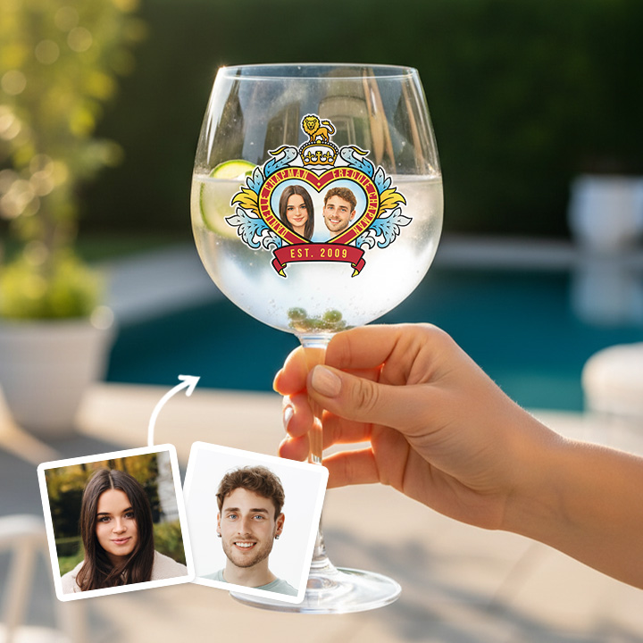 A custom glass with a clear liquid in it boasting a Royal Wedding style love heart design which has been personalised with a picture of a couple alongside their names and date they got married/together with a garden background