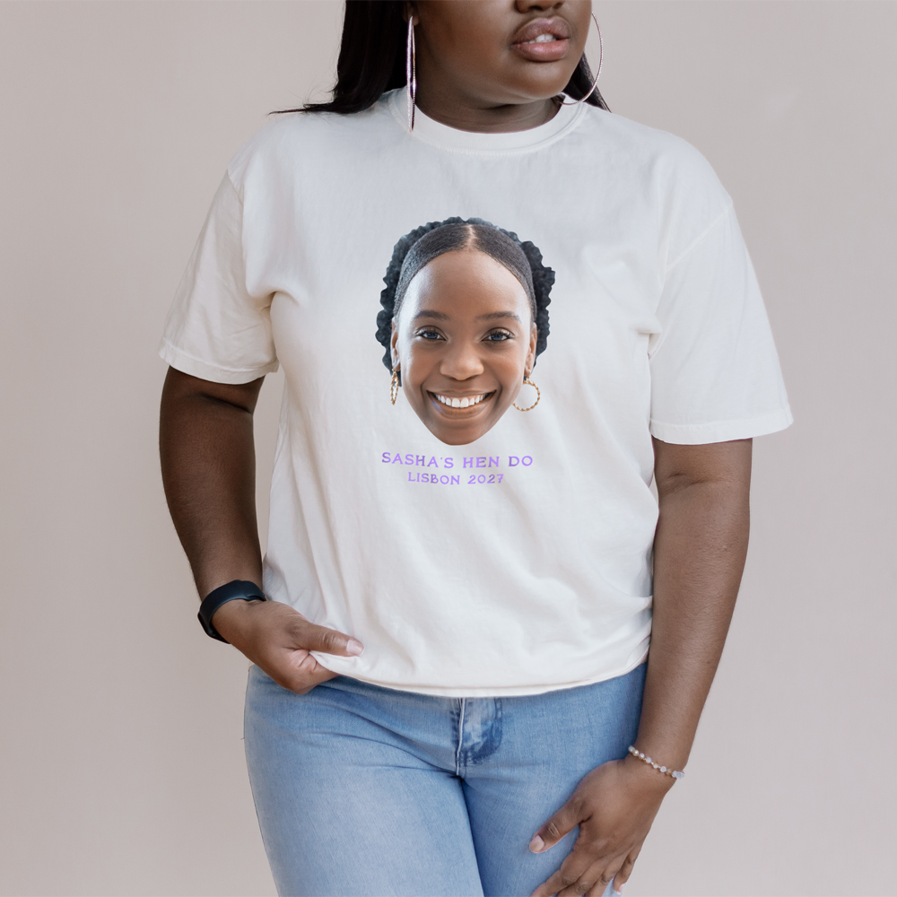 A female model standing in front of a lake wearing a custom hen do t-shirt that has been customised with a picture of a woman's face and the custom text Leanne's Hen Barcelona 2027