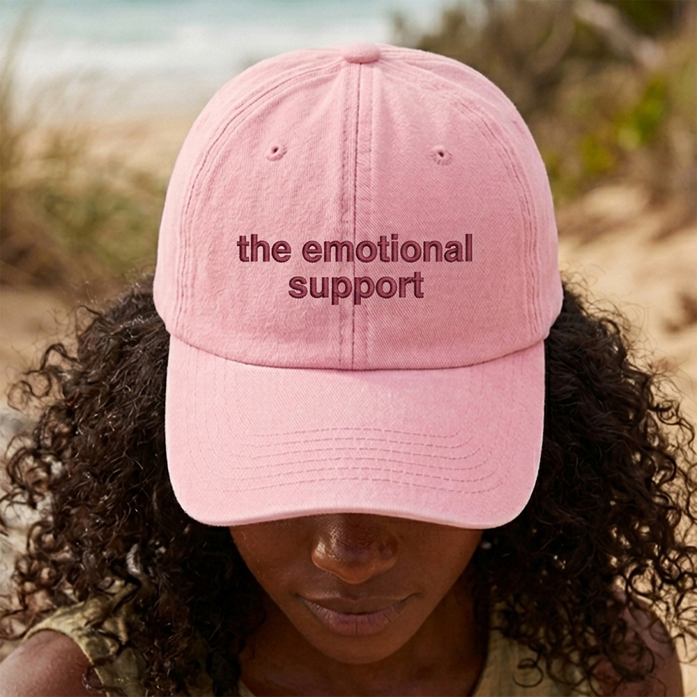 A female model in front of an outdoor background wearing a premium hen do cap in pink that has been embroidered with custom text the emotional support in a red font