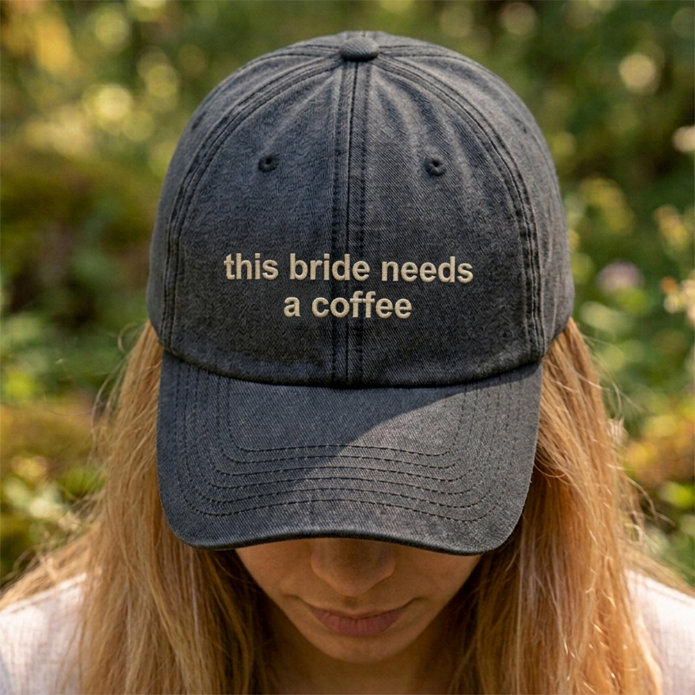 A female model stood in front of an outdoor background with a premium hen do cap in black that has been embroidered with the custom text this bride needs a coffee