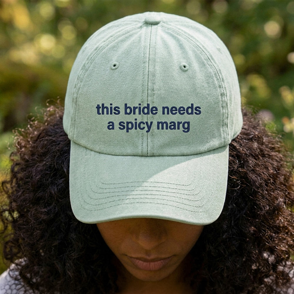 A female model stood in front of an outdoor background with a premium hen do cap in light green that has been embroidered with the custom text this bride needs a spicy marg