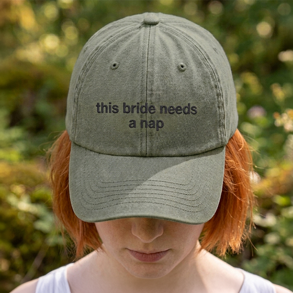 A female model stood in front of an outdoor background with a premium hen do cap in green that has been embroidered with the custom text this bride needs a nap