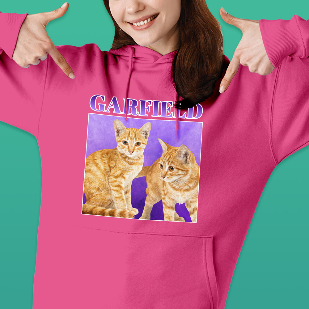 A female model wearing a custom pet hoodie with a bootleg-style design that has the same ginger cat on it twice with custom text reading Garfield