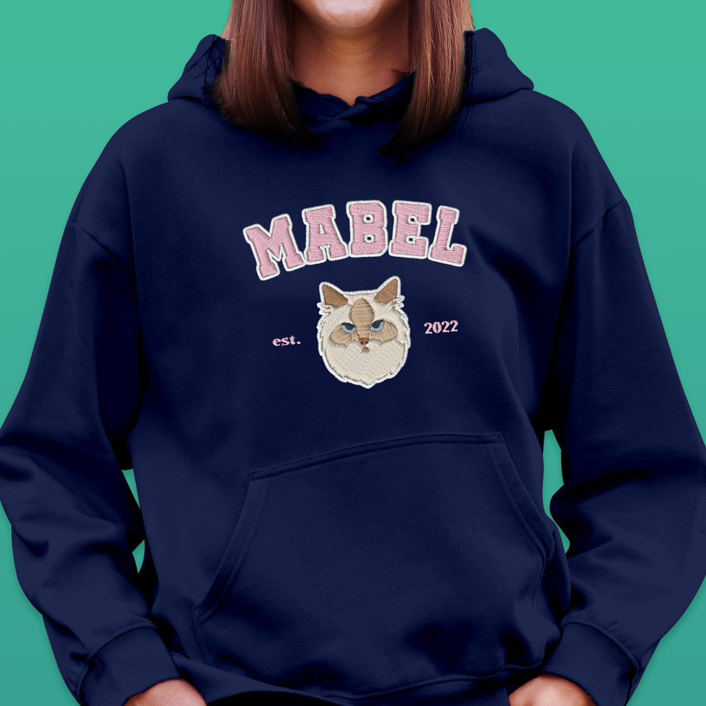 A custom pet hoodie in a varsity style which has been customised with an embroidered cat and custom text reading Mabel est 2022 
