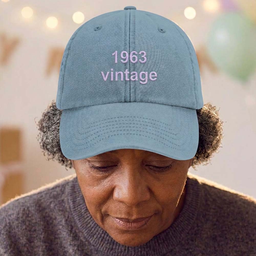 A male model stood in front of a blurred birthday background wearing a premium vintage birthday cap in blue with the custom text 1963 vintage embroidered on it in blue font