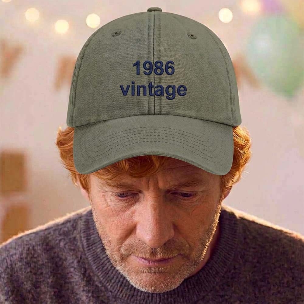 A male model stood in front of a blurred birthday background wearing a premium vintage birthday cap in green with the custom text 1986 vintage embroidered on it in blue font