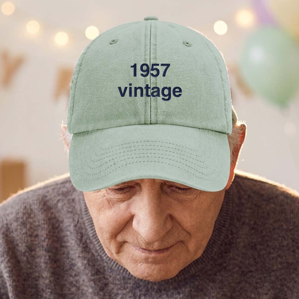 A male model stood in front of a blurred birthday background wearing a premium vintage birthday cap in green with the custom text 1957 vintage embroidered on it in black font