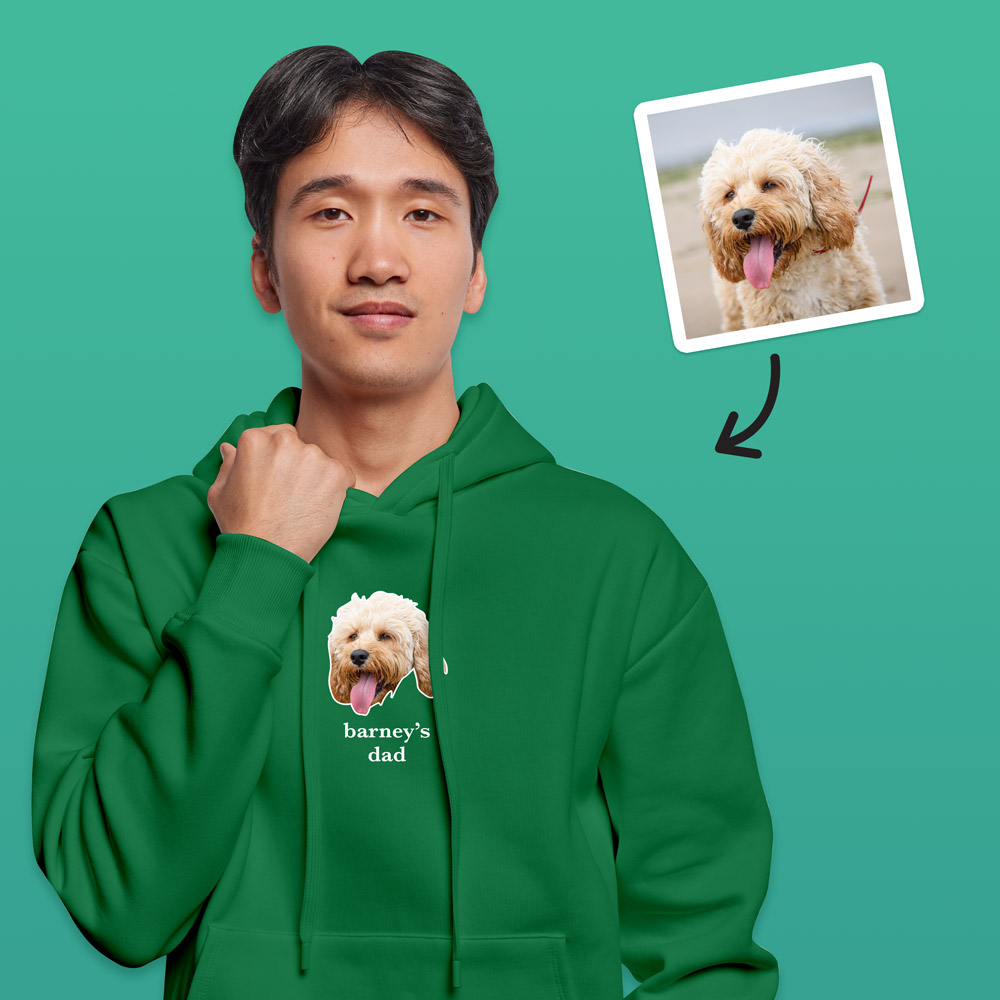 A male model wearing a white hoodie that can be customised with the face of a pet and up to two lines of custom text which has a dog's face on it with the words barneys dad under it