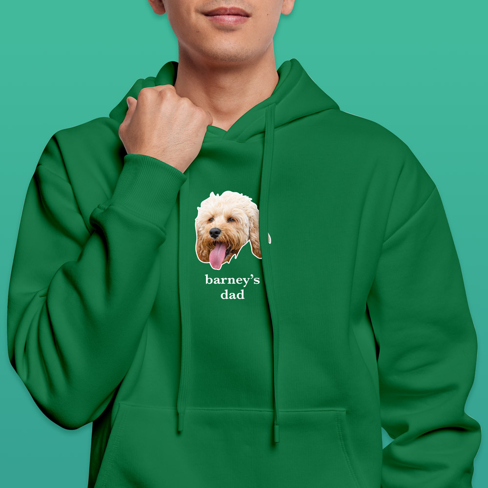 A green hoodie that can be customised with the face of a pet and up to two lines of custom text which has a dogs face on it with the words barney's dad under it 
