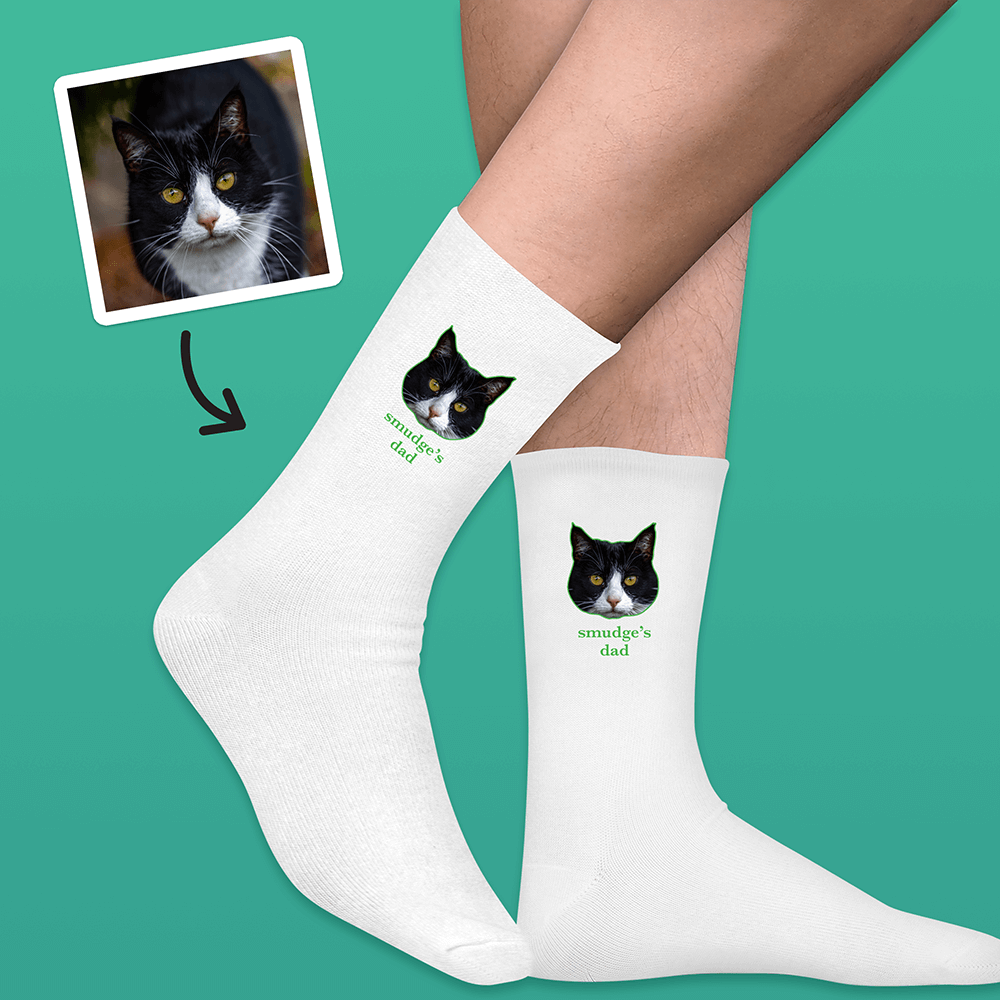 A pair of white socks that can be customised with the face of a pet and up to two lines of custom text that have a picture of a cat on each sock with the words smudge's dad underneath it