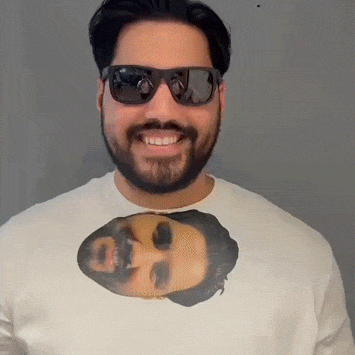 A gif of a man wearing sunglasses who takes them off to put them on his t-shirt collar which makes it look like a sideways pic of him is wearing shades