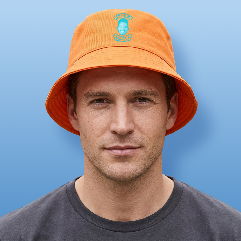 A male model wearing a two tone custom orange stag do bucket hat that has been personalised with a blue face photo and custom text reading Alleh's Stag Do Birmingham 2028