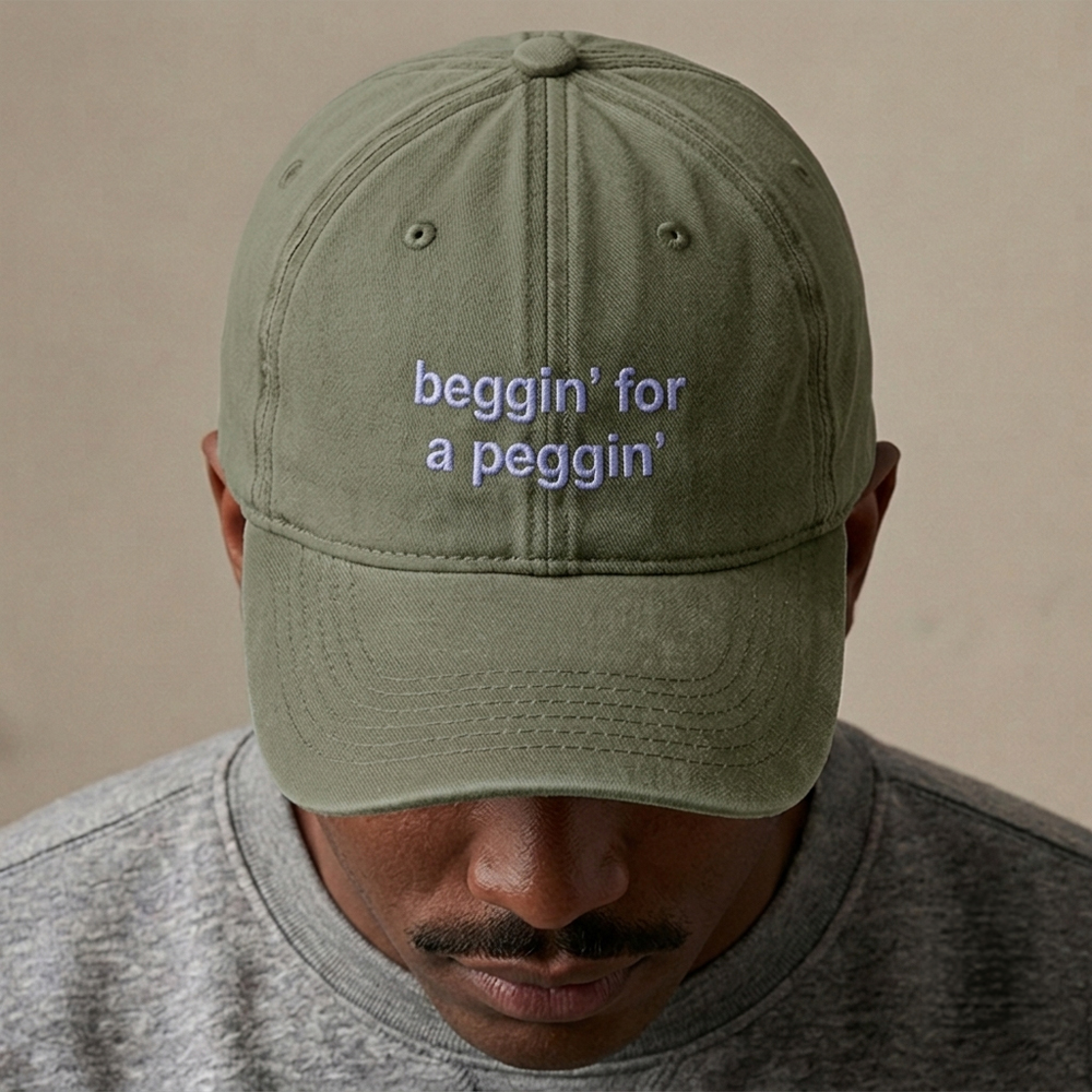 A male model wearing a rude premium vintage cap in bottle green that has been embroidered with beggin for a peggin in light blue coloured thread