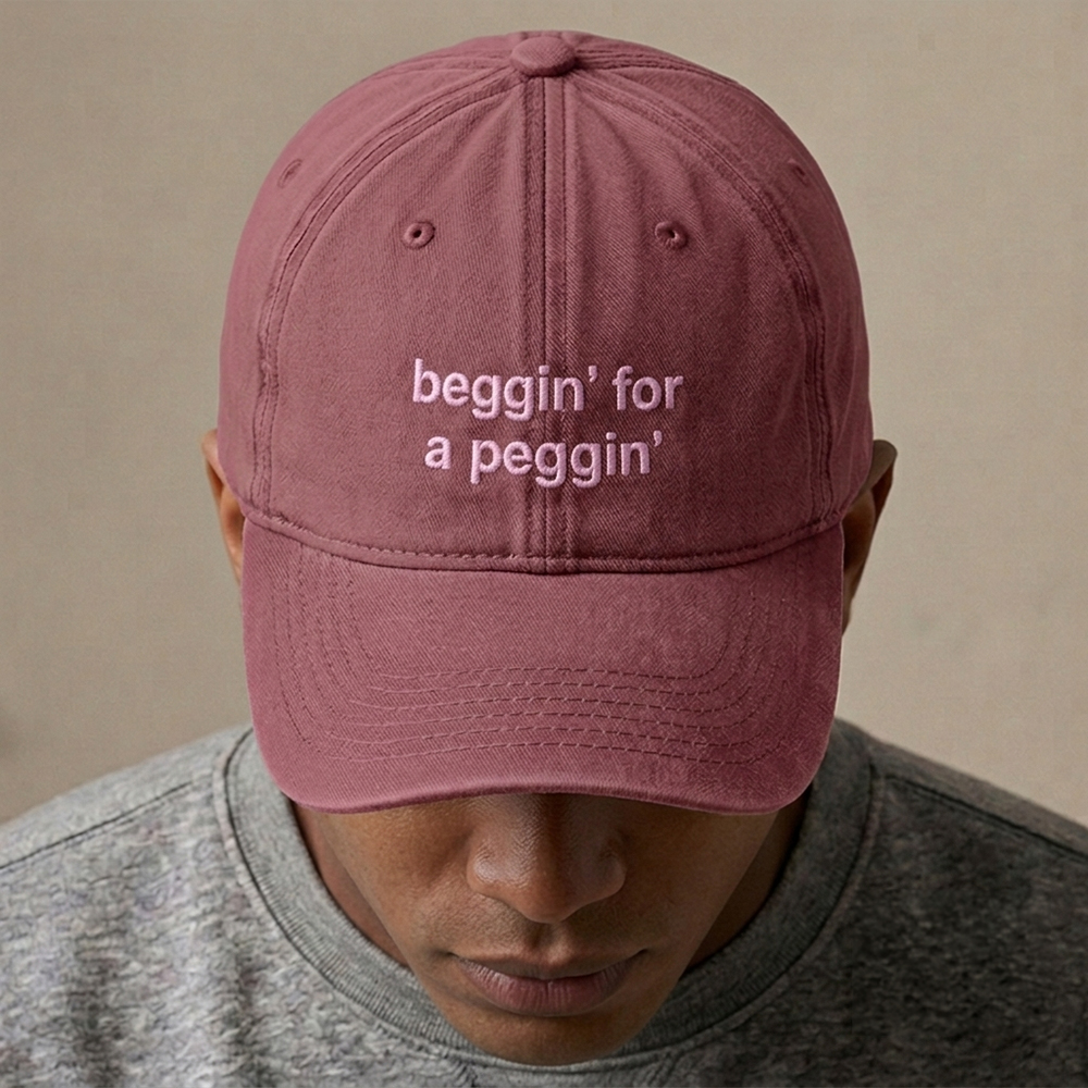 A male model wearing a rude premium vintage cap in red that has been embroidered with beggin for a peggin in pink coloured thread