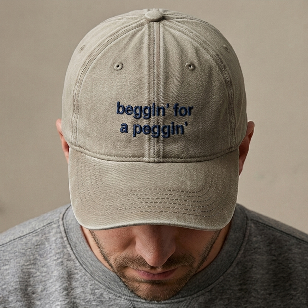 A male model wearing a rude premium vintage cap in sand that has been embroidered with beggin for a peggin in blue coloured thread 