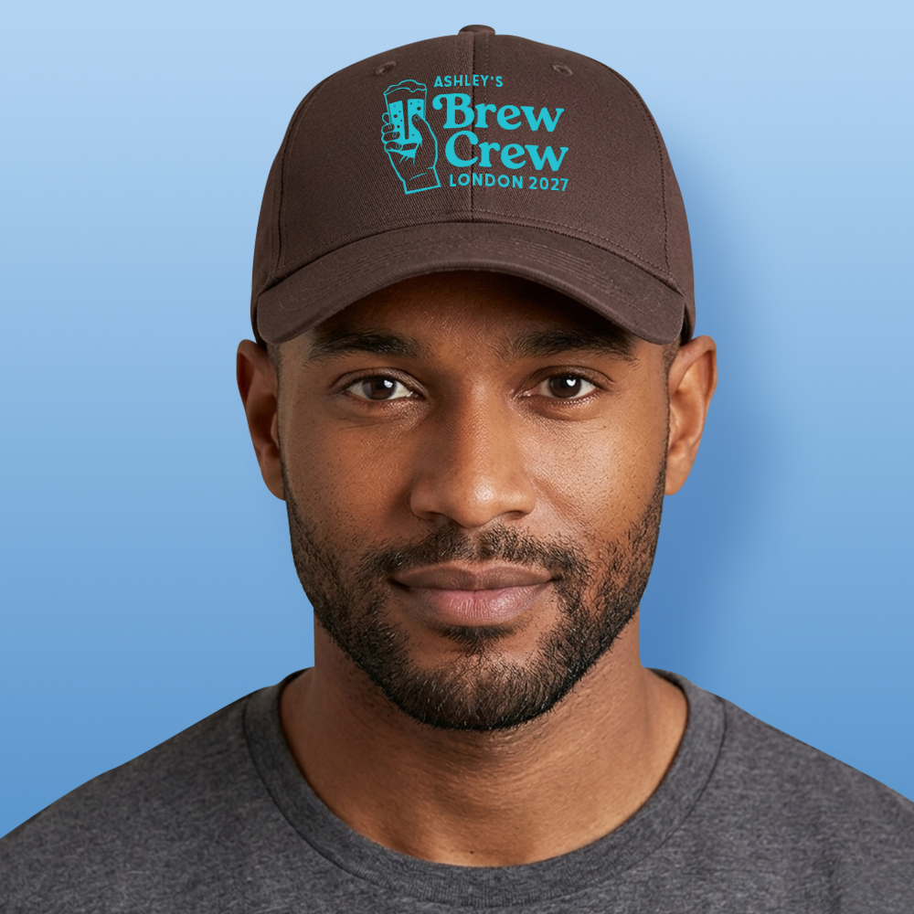 A male model wearing a light blue custom stag do cap with a graphic of a hand holding a beer and custom text reading Ashley's Brew Crew London 2027 in light blue font