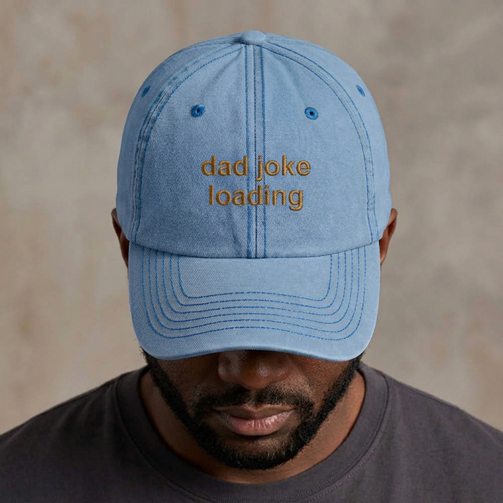A male model wearing a premium vintage cap in blue with the phrase dad joke loading embroidered in toasted almond font