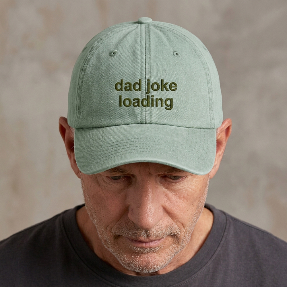 A male model wearing a premium vintage cap in light green with the phrase dad joke loading embroidered in dark green font