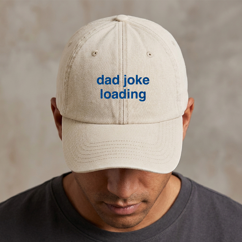 A male model wearing a premium vintage cap in white with the phrase dad joke loading embroidered in blue font