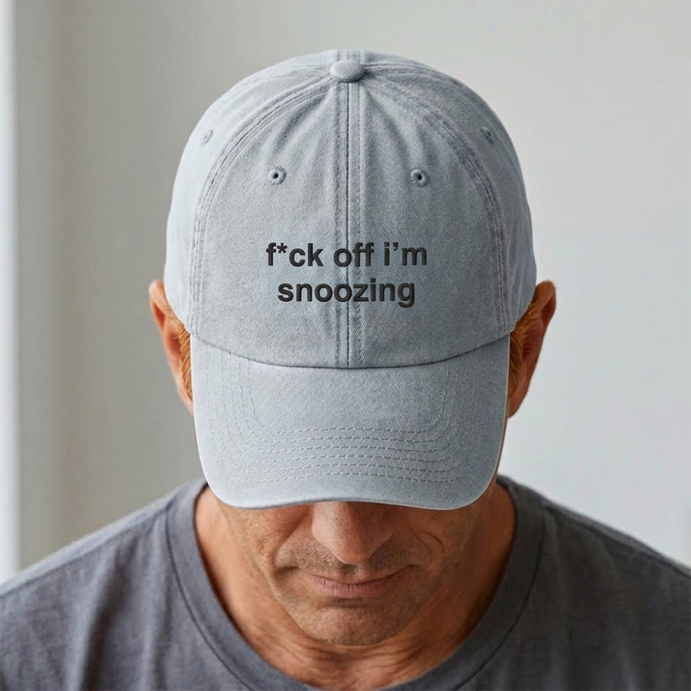 A male model stood in front of a blurred background wearing a premium vintage embroidered cap in blue reading f*ck off i'm snoozing in blue custom text