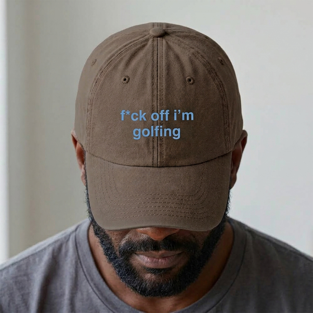 A male model stood in front of a blurred background wearing a premium vintage embroidered cap in brown reading f*ck off i'm golfing in blue custom text