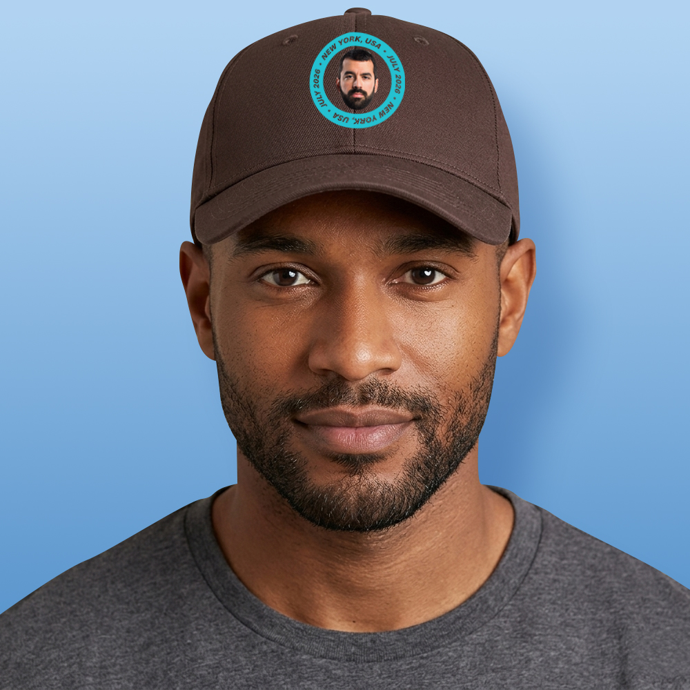 A male model wearing a brown stag do cap that has a circular football badge style design that has been personalised with a photo of a man and the text New York, USA July 2026