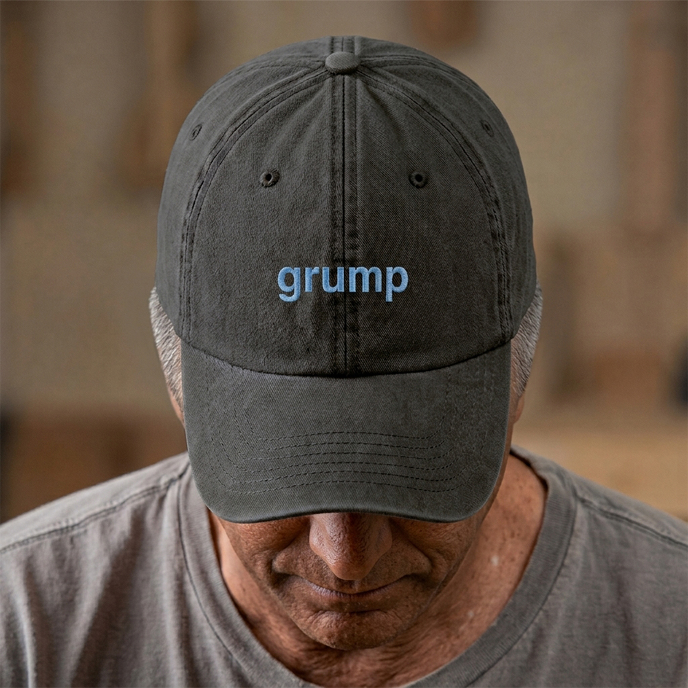 A male model stood in front of a blurred background wearing a premium vintage embroidered Father's day cap in black reading grump in blue text