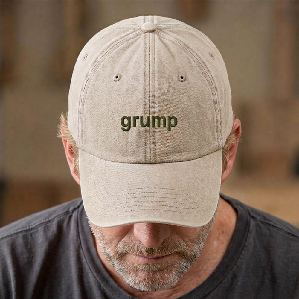 A male model stood in front of a blurred background wearing a premium vintage embroidered Father's day cap in vintage sand reading grump in green text