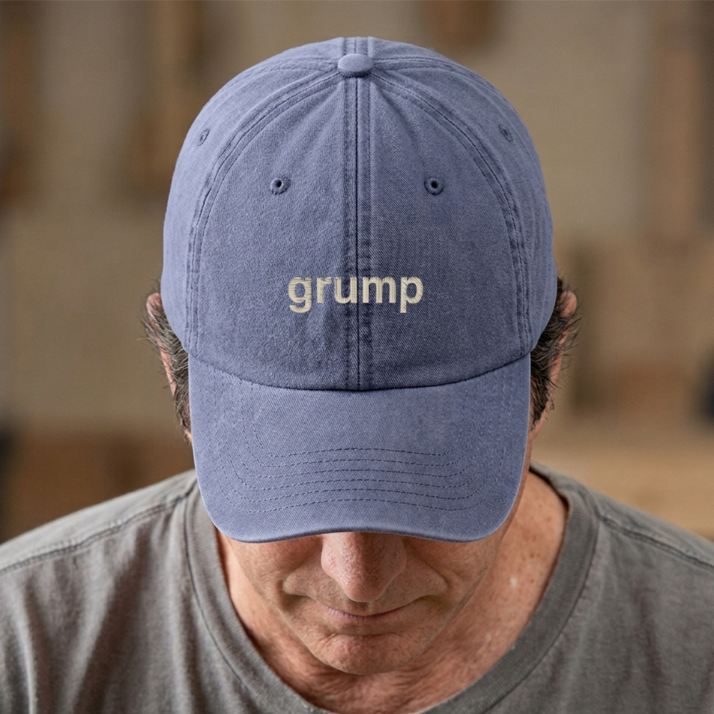 A male model stood in front of a blurred background wearing a premium vintage embroidered Father's day cap in blue reading grump in tusk text 