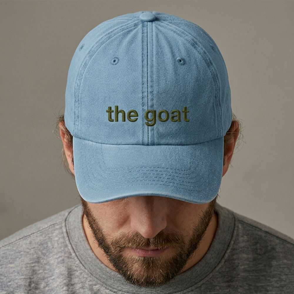 A male model wearing a custom text premium vintage cap in blue that has been embroidered with the nickname the goat