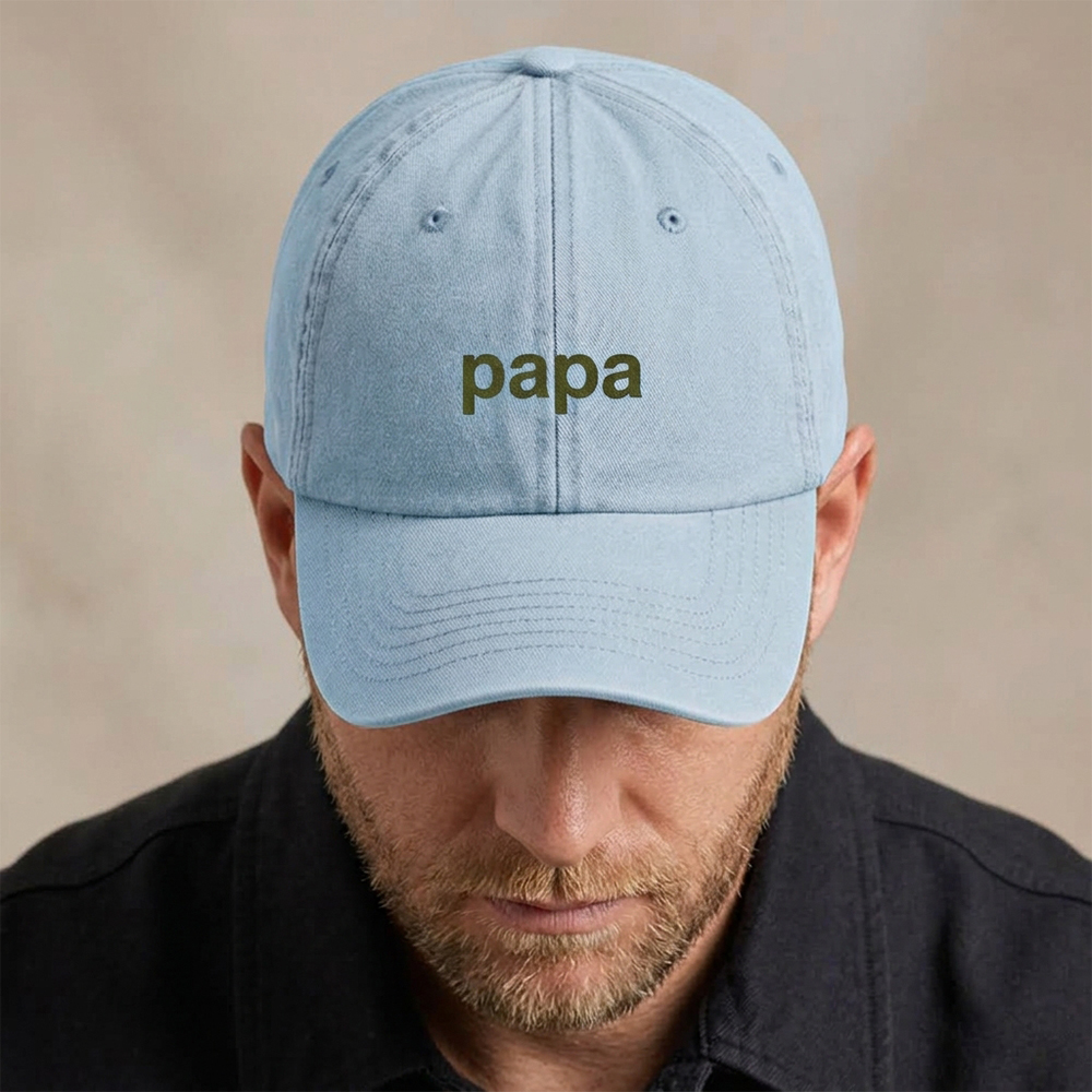 A male model wearing a premium vintage cap Father's Day cap in blue that has been embroidered with the word papa in green font