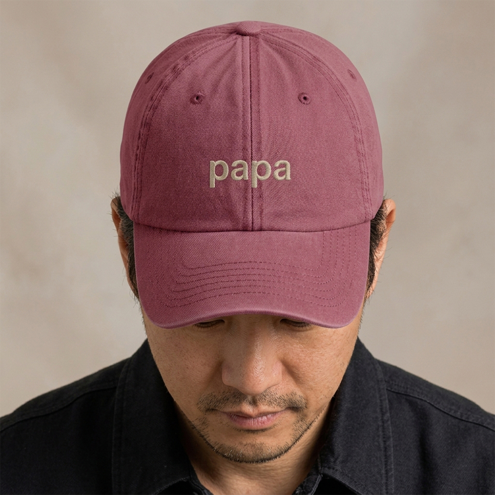 A male model wearing a premium vintage cap Father's Day cap in red that has been embroidered with the word papa in tusk font
