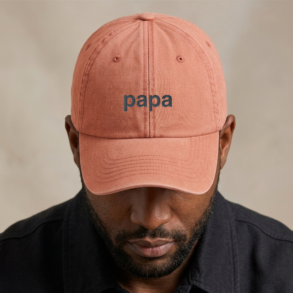 A male model wearing a premium vintage cap Father's Day cap in vintage peach that has been embroidered with the word papa in blue font