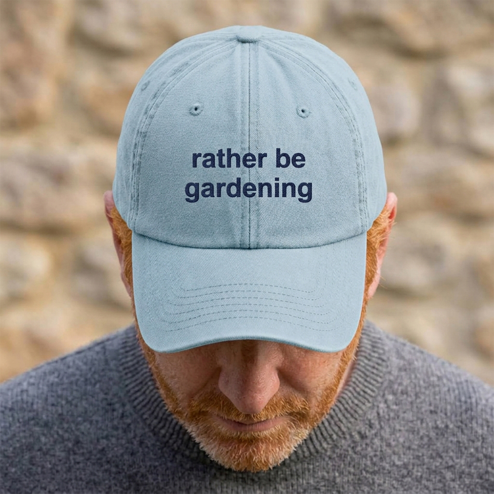 A male model stood in front of a blurred background wearing a premium vintage embroidered Father's day cap in light blue with custom text reading rather be gardening in navy blue font