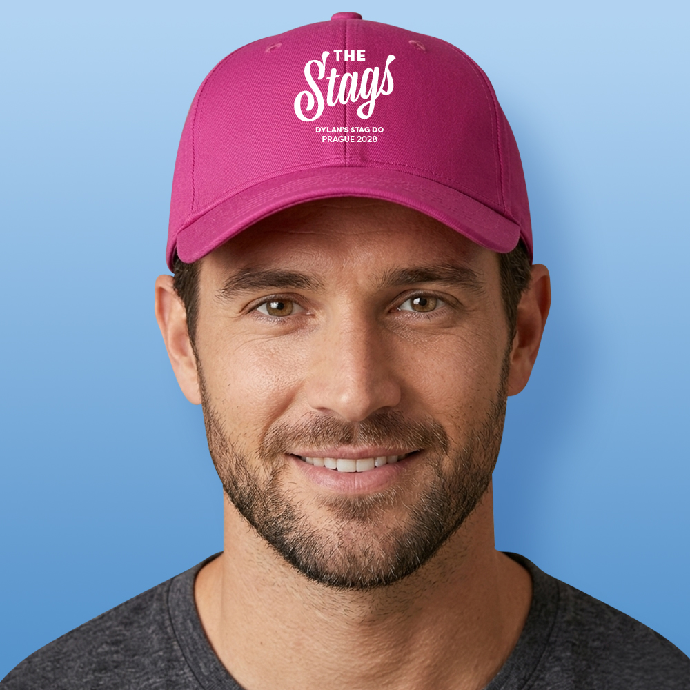 A male model wearing a pink stag do custom cap that reads The Stags in a fancy handwriting font with custom text Dylan's Stag Do Prague 2028 underneath it