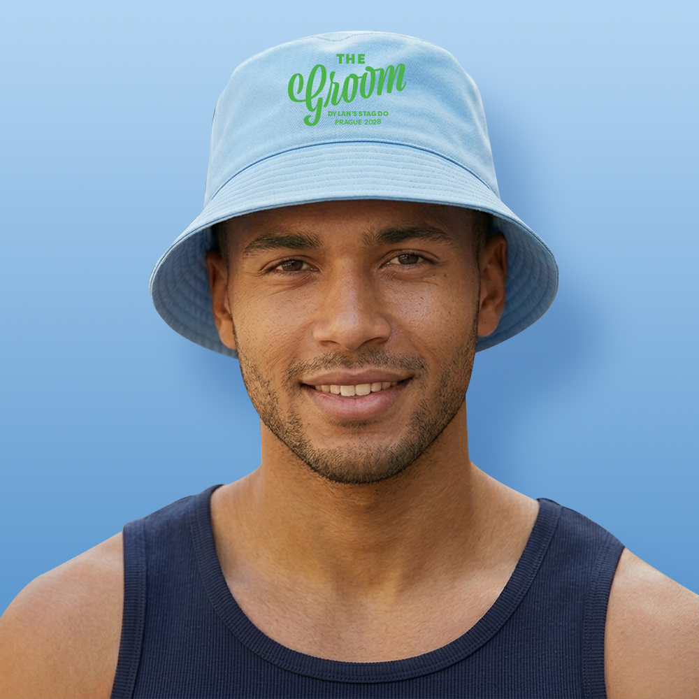 A male model wearing a light blue do custom bucket hat that reads The Groom in a fancy handwriting font with custom text Dylan's Stag Do Prague 2028 underneath it
