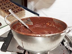 A metal mixing bowl full of melted chocolate with a metal spoon 