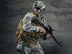 Image of a guy weating camoflague clothing with a helmet and goggles holding a gun