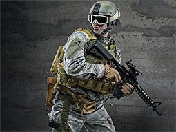 A man wearing army gear with goggles on holding a airsoft gun