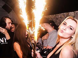People in a club with a woman pouting and holding sparklers in the foreground