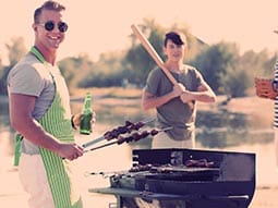 A man wearing sunglasses cooking on a bbq and a man holding a baseball bat